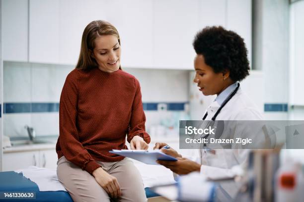 Happy Woman Going Through Her Medical Data With Black Female Doctor At The Clinic Stock Photo - Download Image Now
