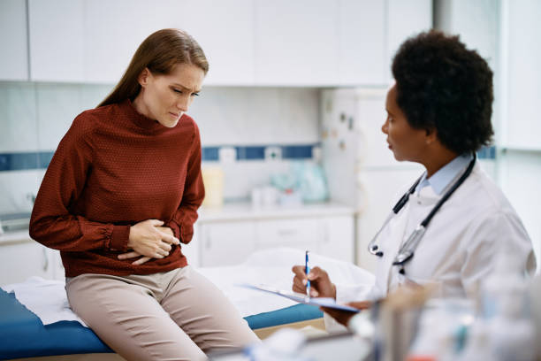 Mid adult woman with stomachache having medical appointment at doctor's office. Female patient holding her abdomen in pain while talking to her doctor at medica clinic. endometriosis stock pictures, royalty-free photos & images