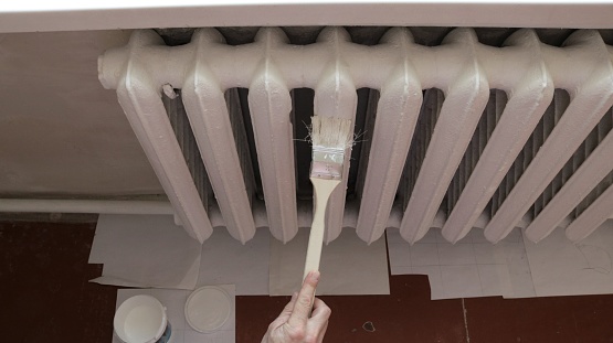 white enamel painting of a retro heating radiator using a long-handled brush to access hard-to-reach places, top view, vintage room batteries in the process of refreshing with white paint