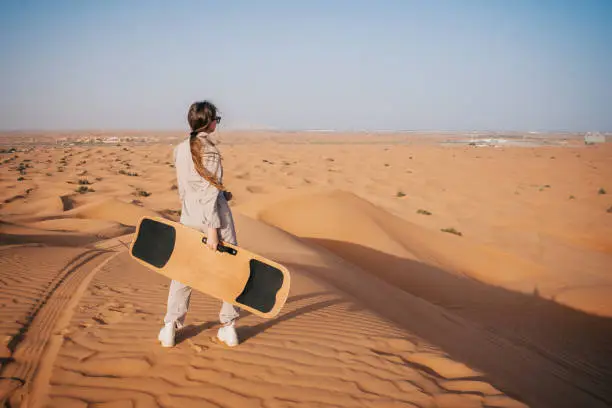 Woman sandboarding in the Dubai desert. Popular tourist attraction.