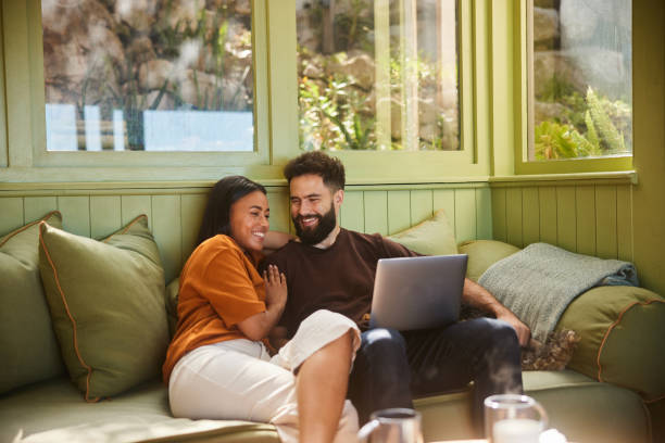 Smiling couple using a laptop while sitting on their sofa with their dog - fotografia de stock