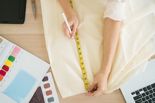 Top view of female fashion designer or tailor hand measuring fabric with measuring tape with example colors of fabrics. Fashion designer tailor in the workshop working for a new collection.