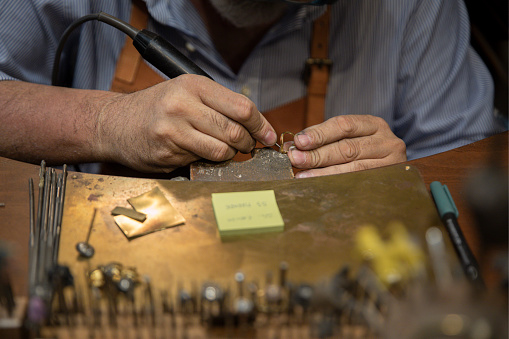 Silversmith working with tools on a jewelers bench in a traditional artisanal silversmith workshop and studio in Centro Storico in Florence, Italy