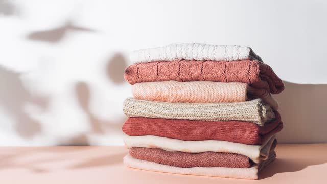 Creative stop motion animation made with pile of textured woolen sweaters in pastel colors against sunlit white background. Autumn and winter fashion aesthetic.