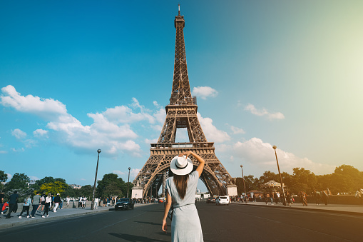 Rear view of woman tourist in sun hat standing in front of Eiffel Tower in Paris. Travel in France, tourism concept. Holiday or vacation in Paris. High quality photo