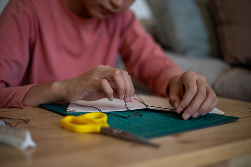 An inventive young woman making her own notebook by using leftover paper and sewing it with thread.