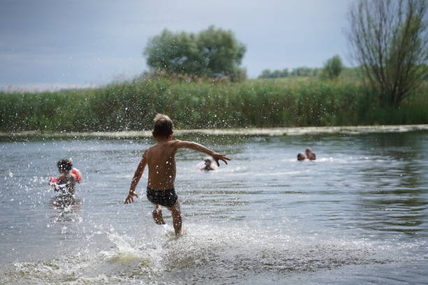 Children jumping from stone beach to beautiful blue lake. Having fun with your friends on summer vacation.