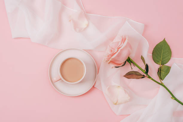 istock A coffee cup and pink rose on white silk fabric. Holiday concept. Top view, flat lay 1461343505