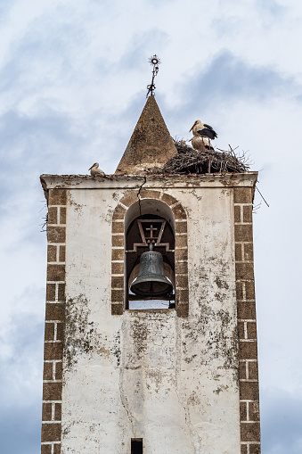 Nest of storks on top of old stone bell tower with iron cross at Herreruela, Extremadura in Spain. Paradise for storks.
