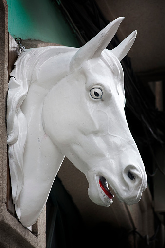 Horse head sculpture seen in the street, store sign.