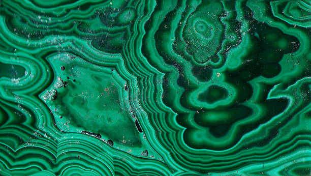 Texture of Natural Malachite stone with little touch of digital imaging Malachite is a copper carbonate hydroxide mineral, with the formula Cu2CO3(OH)2. This opaque, green-banded mineral crystallizes in the monoclinic crystal system, and most often forms botryoidal, fibrous, or stalagmitic masses, in fractures and deep, underground spaces, where the water table and hydrothermal fluids provide the means for chemical precipitation. Individual crystals are rare, but occur as slender to acicular prisms. Pseudomorphs after more tabular or blocky azurite crystals also occur. malachite stock pictures, royalty-free photos & images