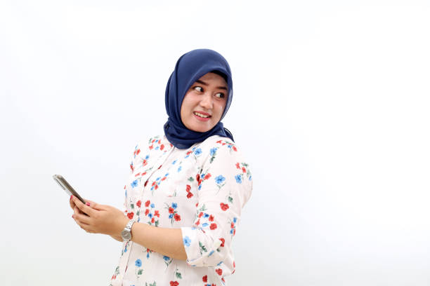 istock Happy asian muslim woman holding a cell phone while looking back. Isolated on white background 1461348152