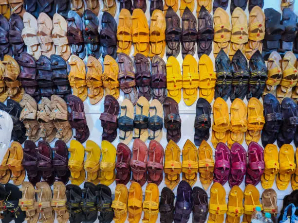 Photo of Stock photo of popular and traditional kolhapuri chappal display on wall for sale in the local shop.It is handmade leather chappal with unique design and color at Kolhapur, Maharashtra, India.