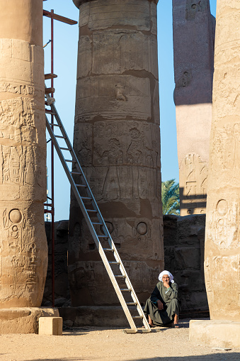 LUXOR, EGYPT - 27 Dec 2022. Old african man with white turban sitting inside a temple with a ladder and columns around