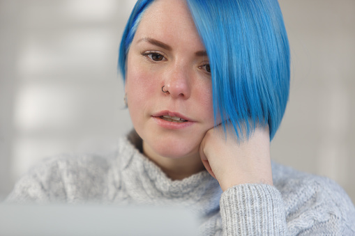Young adult female person with dyed blue hair works on modern computer at home as a freelancer