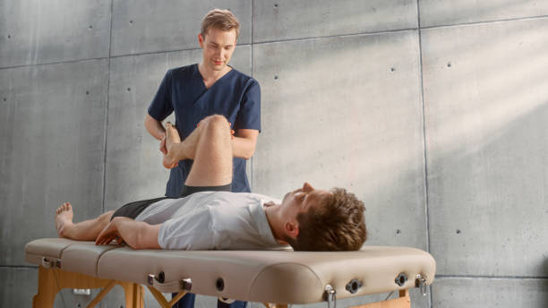 istock Sport Physiotherapy Specialist Stretching and Working on Specific Muscle Groups or Joints with Young Male Athlete. Sportsman Recovering from Mild Injury, Undergoing Rehabilitation. Healthcare Concept. 1461352893
