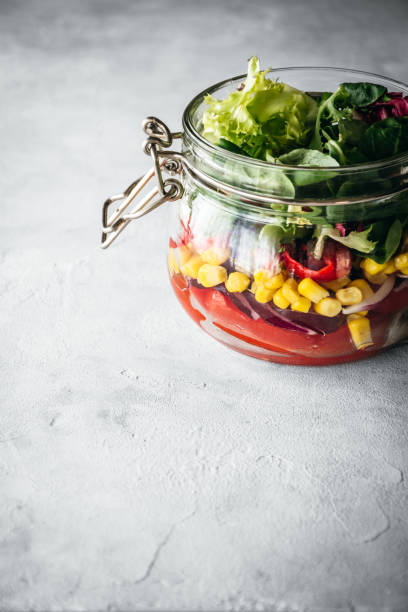 Salad with corn, lettuce, tomato and red pepper in a glass jar. Healthy food to take to work.