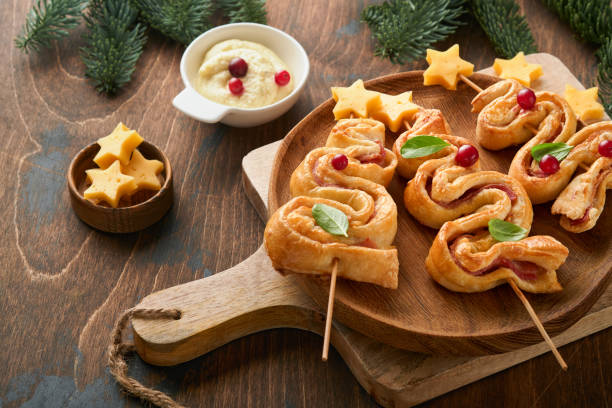 Christmas or New Year appetizer. Christmas tree shape puff pastry buns with cheese and ham. Group of Christmas tree shapes on wooden board. Festive idea for Christmas or New Year dinner. Top view.