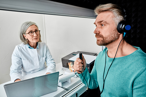 Male patient wearing audiology headphones pressing button of response while audiometric testing in soundproof audiology booth. Hearing testing