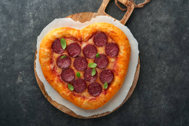 istock Valentines day heart shaped pizza with mozzarella, pepperoni and basil, wine bottle, two wineglass, gift box on black background. Idea for romantic dinner Valentines day. Top view. Mock up. 1461356932