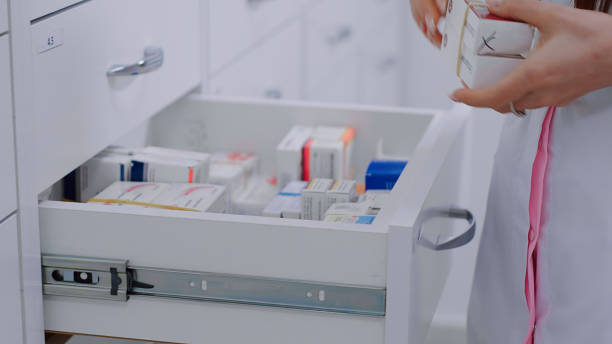Pharmacist puts pills packages in the white drawers