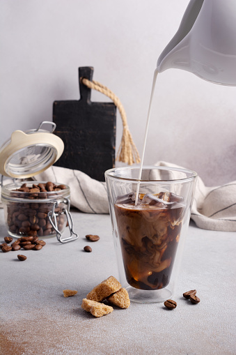 Homemade ice latte. Black coffee with ice and milk or cream in glass for tasty and refreshing break on grey kitchen background