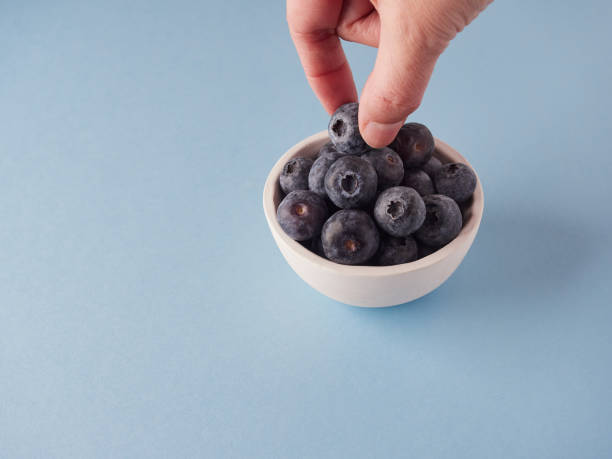 istock hand picking a blueberry from a small bowl on blue surface with copy space 1461369671