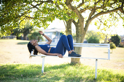 African woman exercising outdoors using smart watch and wireless headphones.