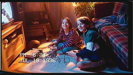 Retro VHS Tape Effect Home Video Concept: Young Brother and Sister Playing Old-School Arcade Video Game on a TV Set and Console at Home. Happy and Excited Kids and Smile to Camera.
