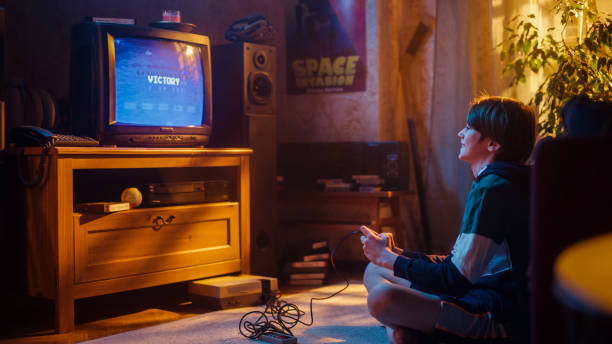 istock Young Boy Playing 80s Eight Bit Arcade Space Shooter Video Game on a Console at Home in His Vintage Room with Old-School Interior. Child Successfully Wins the Level. Nostalgic Retro Childhood. 1461376879