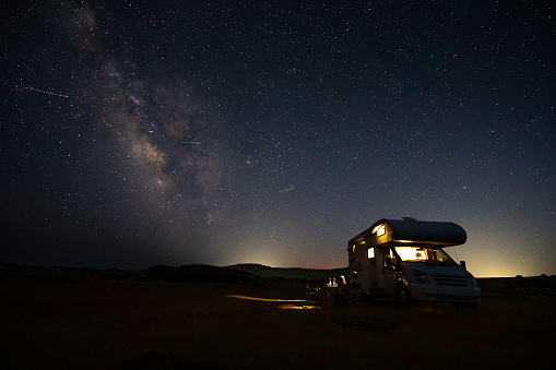 Motorhome RV parked under stars on a pier by the sea, Crete, Greece. Travelers with camper van are resting overnight under milky way on an active family vacation, Crete, Greece.