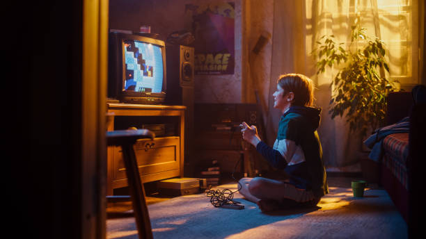 istock Young Boy Playing Eighties Eight Bit Arcade Video Game on a Gaming Console at Home in His Room with Old-School Interior. Child Successfully Wins the Level. Nostalgic Childhood Concept. 1461377149