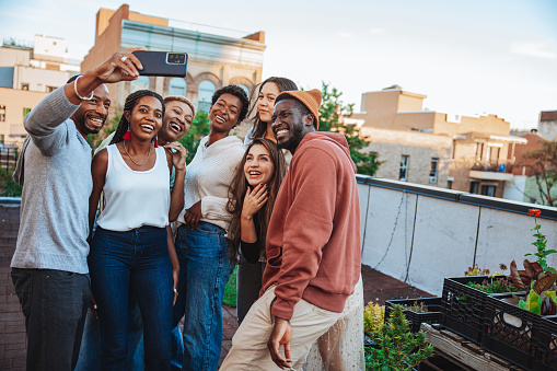 Happy group of friends at a rooftop party take a selfie together.