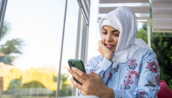 Beautiful Happy Muslim Arabic Woman Using Smartphone Indoors. Concept of social media, online shopping, mobile app