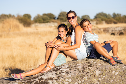 Mother with two kids sitting on a rock at summer
