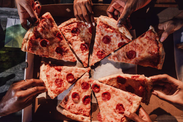 Group of mixed age range friends dining with a pizza on a Brooklyn rooftop.