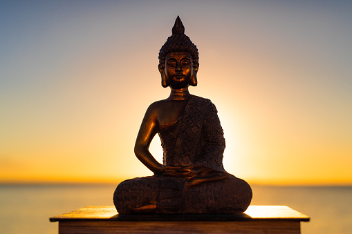 Buddha half silhouette with a real bright shining sunrise by the sea in the background. For zen, mindfulness and other spiritual concepts.