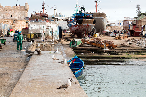 Marrakesh, Morocco - January 27, 2020: Blue-collar workers repairing fishing boats in harbor of Marrakesh, Morocco.