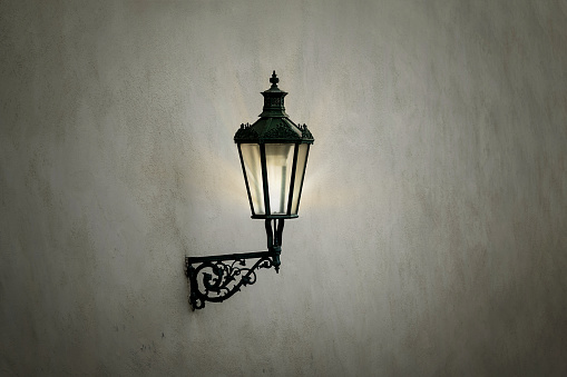 Vintage iron lantern hanging on concrete wall in evening time. Old lamp illuminating urban street.