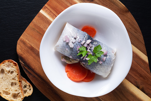 Food concept roll Pickled Herring in white bowl on black background with copy space
