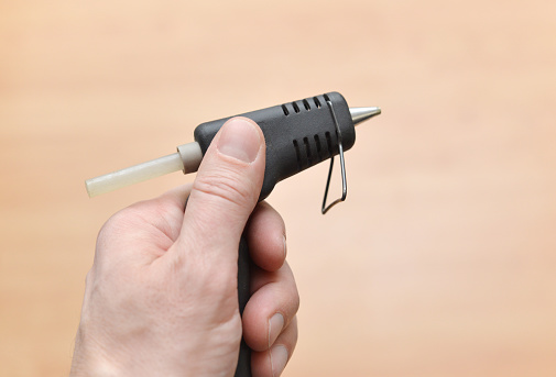 Closeup of a man's hand holding a mini glue gun.