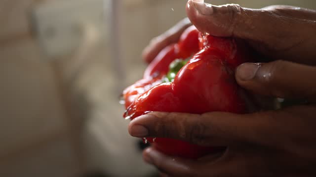 Male hands washing a red bell pepper in the kitchen