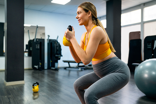 Young pregnant Caucasian woman, exercising in the gym while using small weights