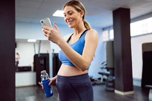 Young pregnant Caucasian woman, using mobile phone in the gym