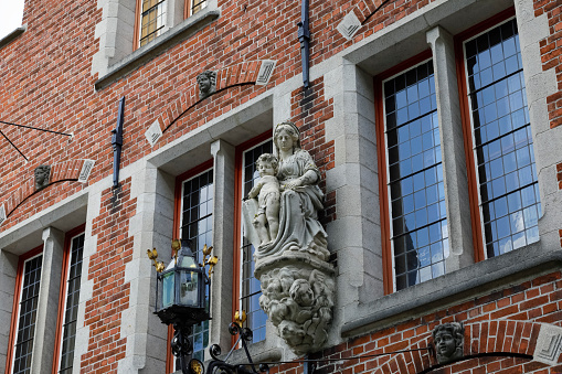 Bruges, Belgium - September 11, 2022: The facade of a historic building with an architectural detail depicting human figures in the form of a small statue