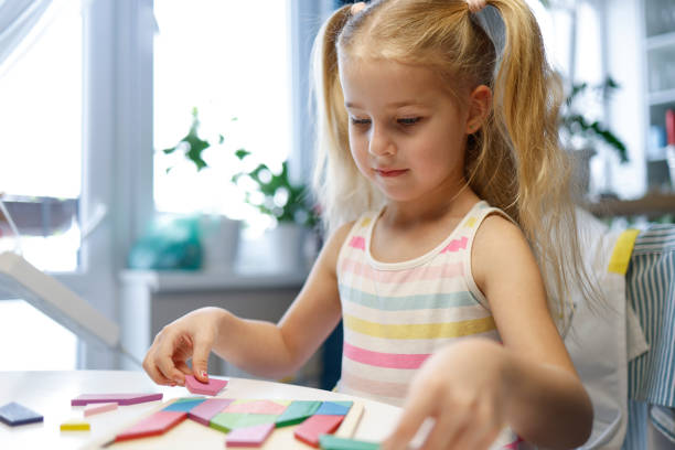retrato de una niña sonriente y feliz jugando con el rompecabezas tangram, con un enfoque superficial: enfoque selectivo en su rostro. - tangram casa fotografías e imágenes de stock