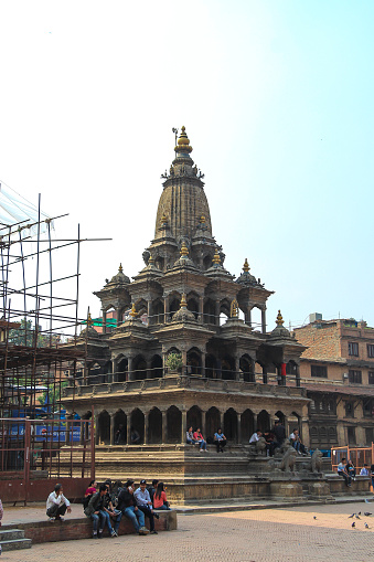 Nepal, Lalitpur - May 10, 2019: Side view of stone Krishna Mandir hindu temple (Shikhara style) on Patan Durbar Square in sunny day. People on the street. Religious architecture. Travel in Asia theme.