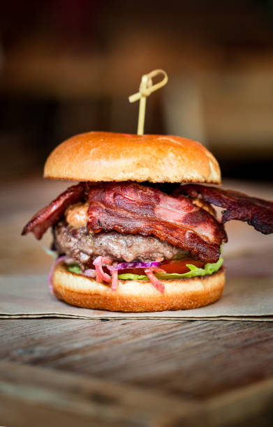 Freshly flame grilled bacon burger in gourmet restaurant Close up image depicting a freshly cooked bacon burger in a restaurant. The burger is loaded with flame grilled beef burger and crispy bacon and salad. bacon cheeseburger stock pictures, royalty-free photos & images