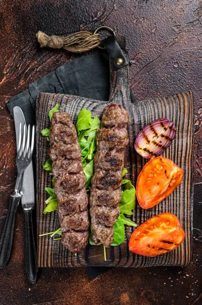 Turkish adana kebab, ground beef and lamb meat grilled on skewers  served with tomato, salad and onion. Dark background. Top view.