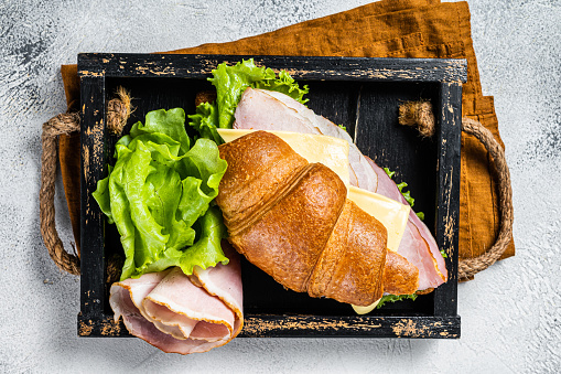 Fresh croissant sandwich with ham, cheese and salad leaf. Gray background. Top view.
